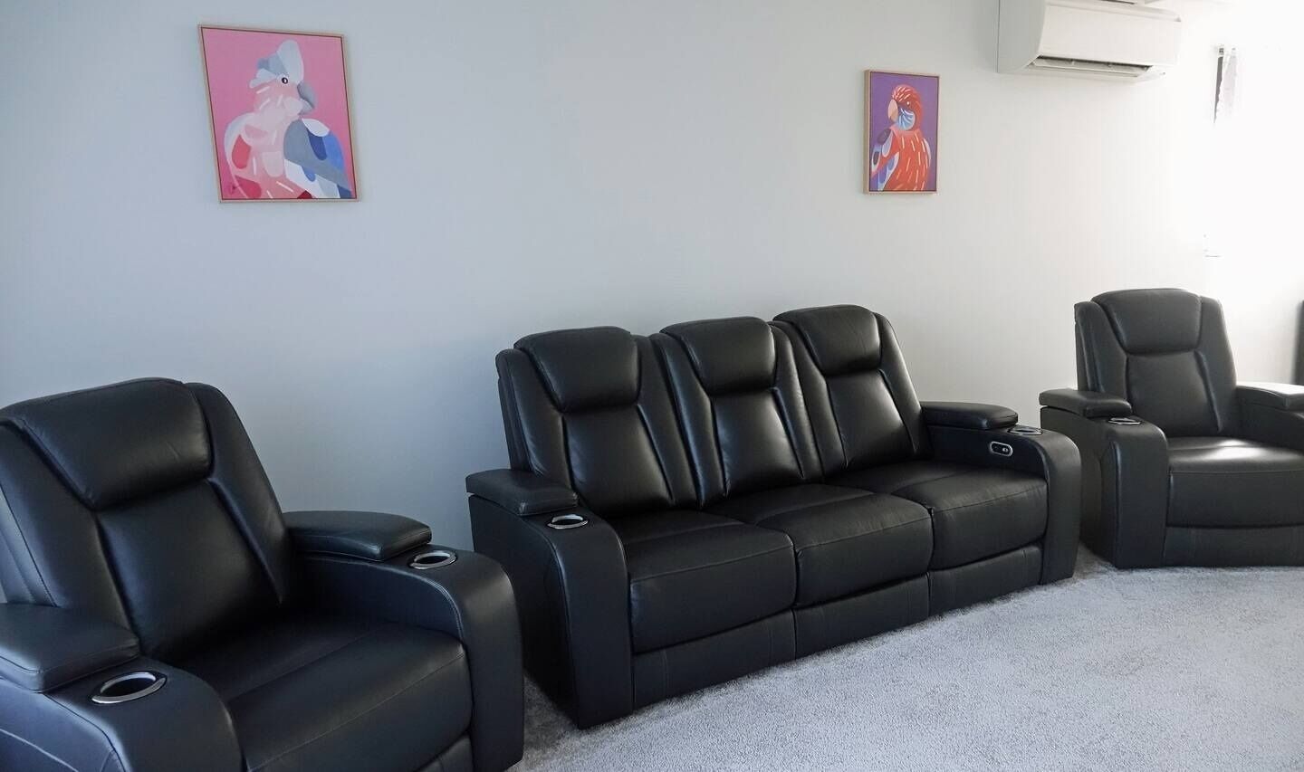 Ein Zimmer mit drei schwarzen Ledersofas und einem einzelnen Sessel, die halbkreisförmig vor einer Wand mit zwei gerahmten Kunstwerken angeordnet sind.