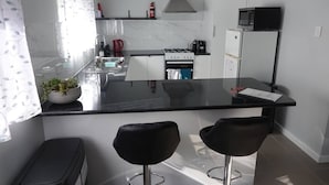 Een moderne keuken met een zwart aanrecht, witte kastjes, een gasfornuis, een magnetron en twee zwarte barkrukken.