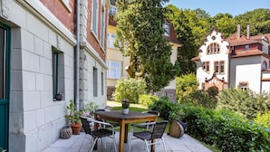 Eine Terrasse mit Tisch und Stühlen, umgeben von Grünflächen und Gebäuden.