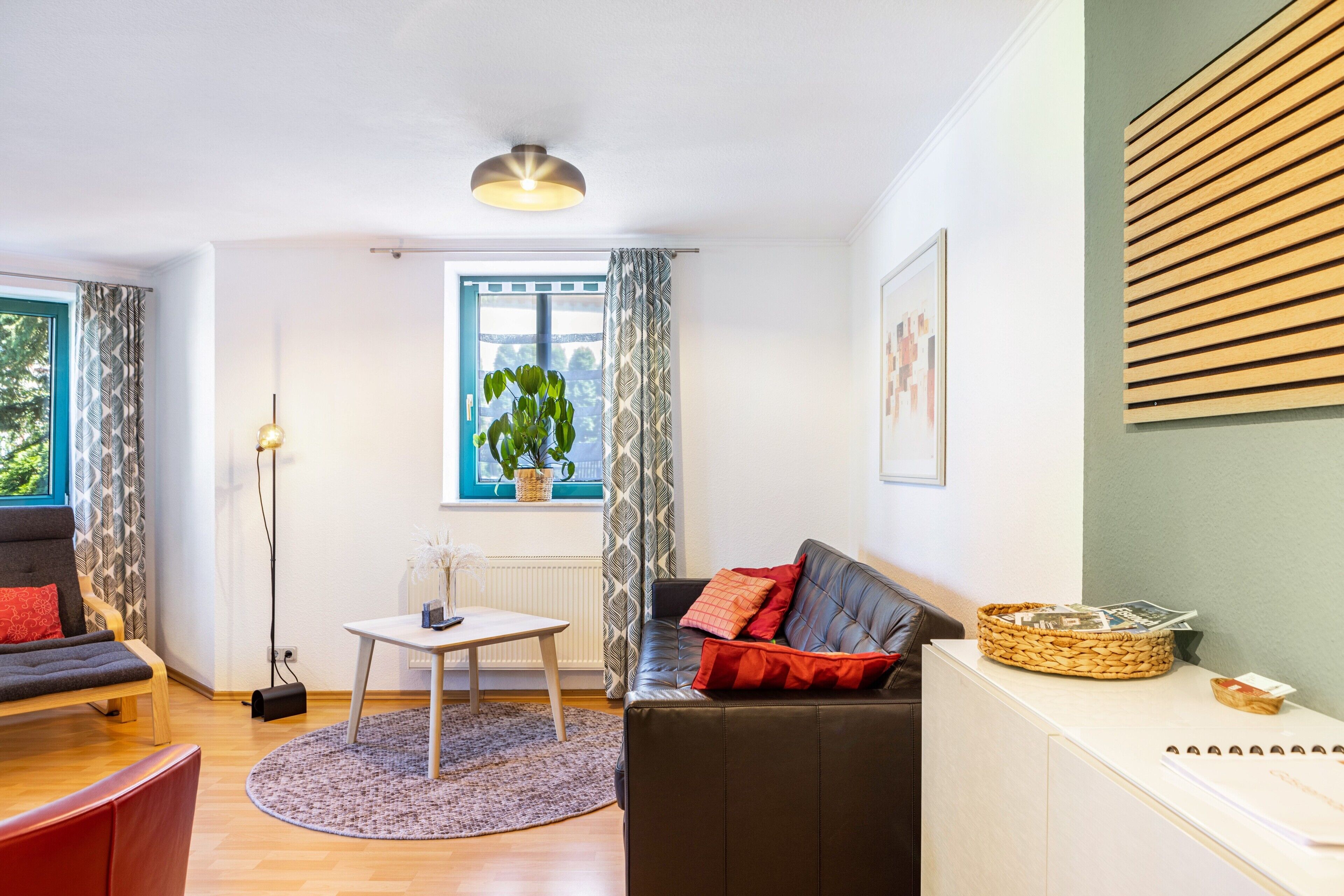 A living room with a sofa, a table, a floor lamp, a window with curtains, and a plant.