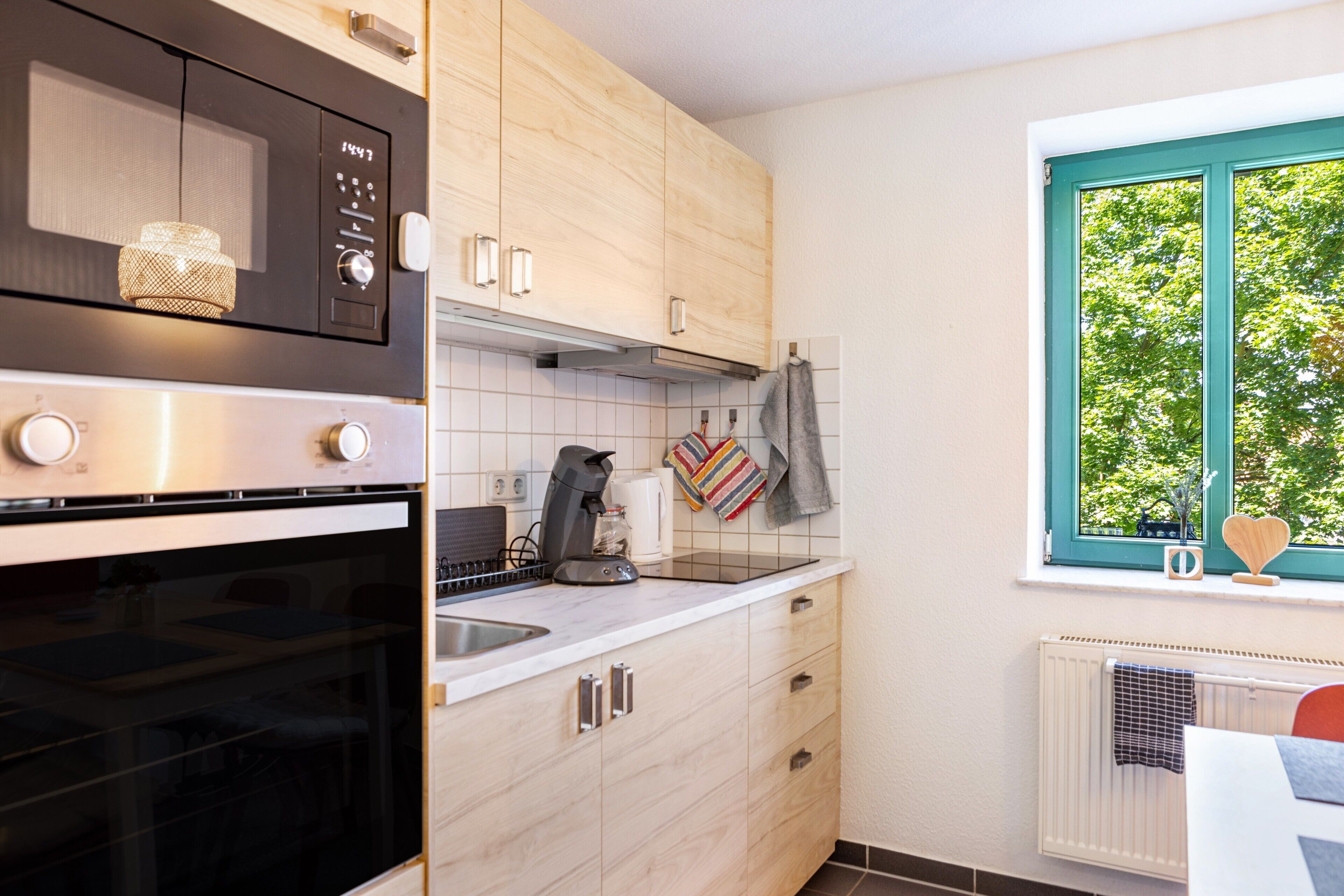 A kitchen with a built-in oven, a coffee maker, and a window with a view of trees.