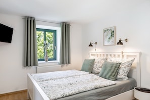 Une chambre à coucher avec un lit, des rideaux, un téléviseur fixé au mur, une fenêtre donnant sur un paysage agréable et une lampe fixée au mur.