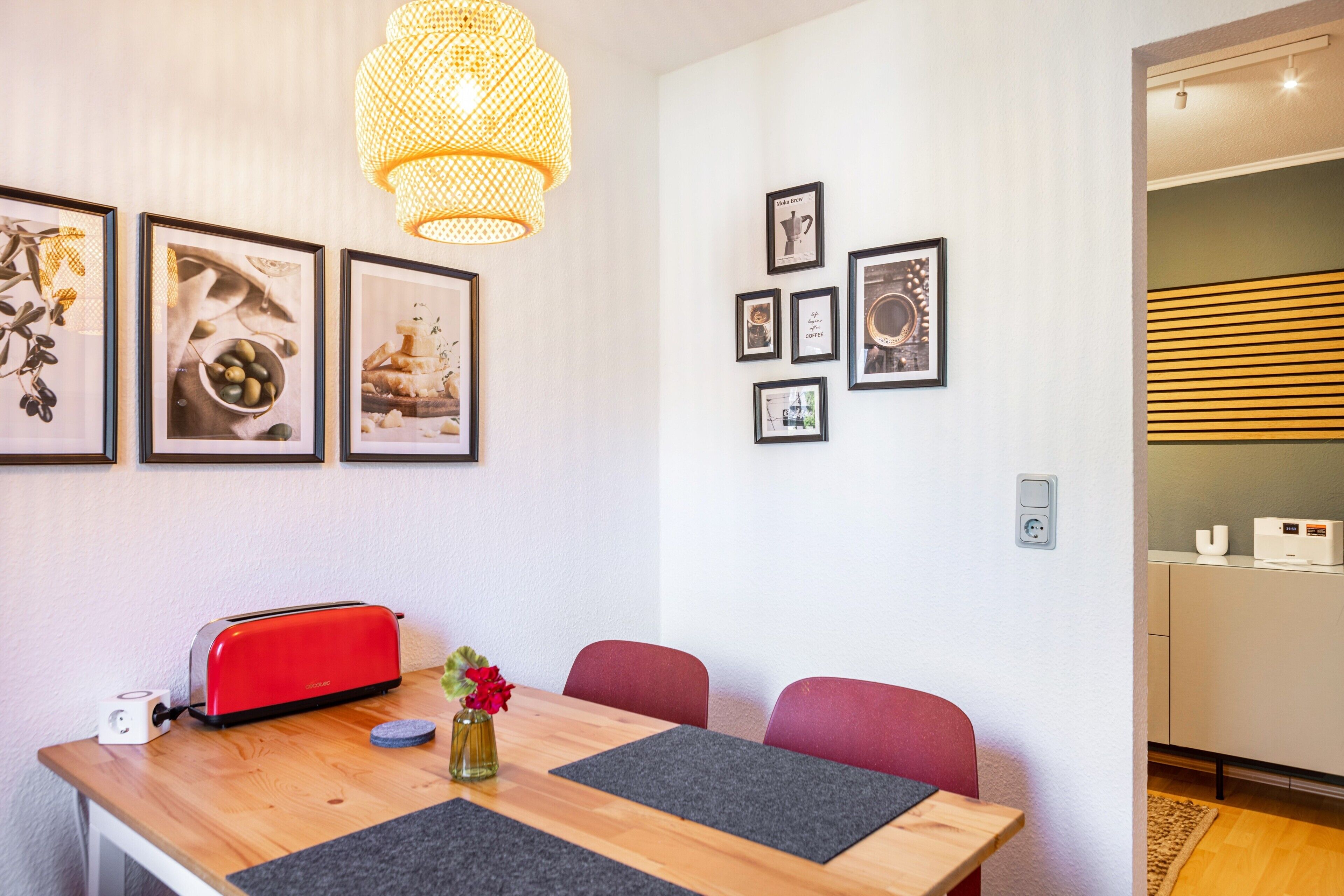 Un comedor con una mesa de madera, sillas rojas, un tostador rojo y una lámpara colgante.