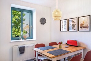 Un coin repas avec une table, des chaises, un grille-pain rouge, une horloge et des tableaux encadrés au mur.