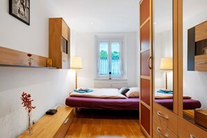 Quarto com cama, abajures, cômoda, espelho e janela com vista para o verde.