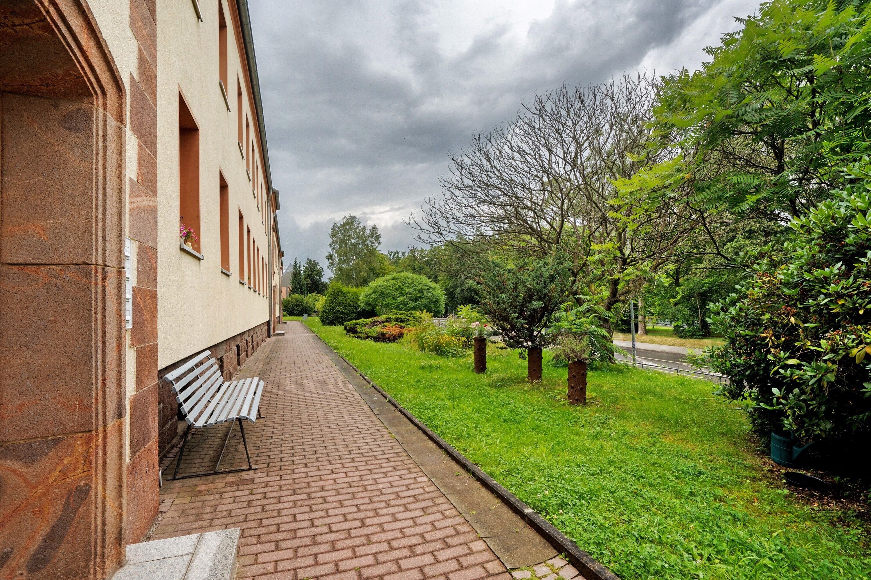 A brick pathway leading to a building with a bench.