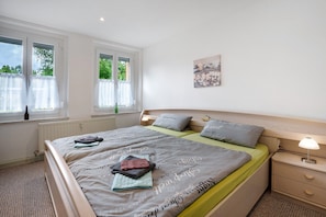 A bedroom with a bed, two bedside tables, a window with curtains, and a wall-mounted artwork. - Holiday Apartment 'Gästewohnung Am Schwanenteich' with Wi-Fi (Mittweida)