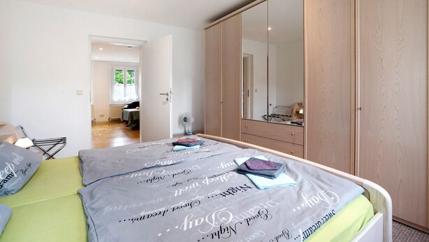 A bedroom with a bed, a wardrobe, and a large mirror.
