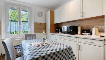 Cuina amb armaris blancs, microones, cafetera i finestra amb cortines.