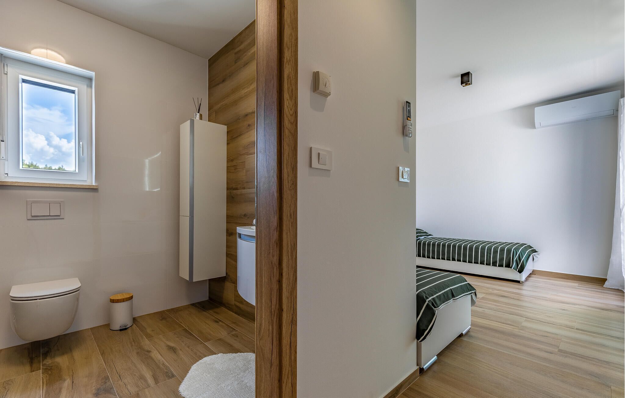 Une chambre à coucher de taille réduite, avec un lit simple, une petite fenêtre, des toilettes et un mur recouvert de panneaux de bois.