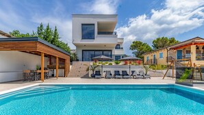 Een modern huis met twee verdiepingen en een zwembad op de voorgrond.