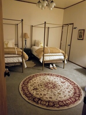 A bedroom with two four-poster beds, a round patterned rug, and a lamp on a nightstand.