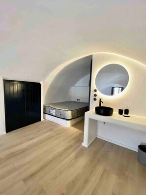 A modern bedroom with a bed, a round mirror, a sink, and a dark wardrobe.