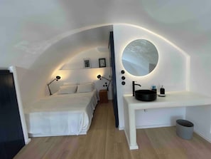 A bedroom with a bed, bedside lamps, a mirror, and a sink.
