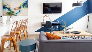Moderni olohuone, jossa on sohva, ruokapöytä, tuoleja, televisio ja työpöytä.