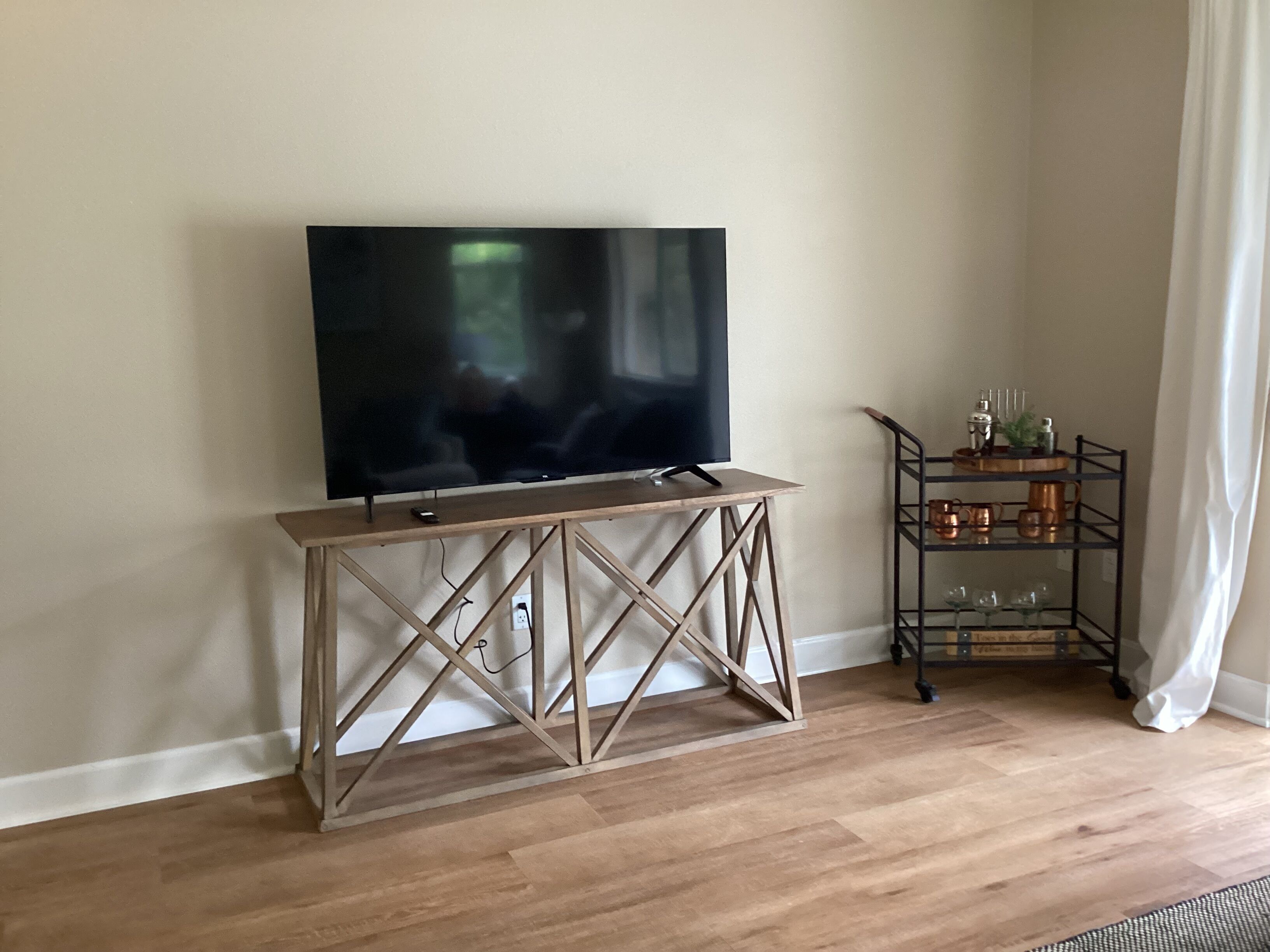 A room with a wooden console table holding a flat-screen TV, a metal shelf with kitchenware, and a wooden floor.