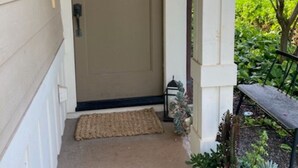 A beige front door with a small window, a black lantern, and a bench outside.