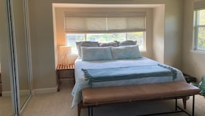 A bedroom with a bed, bench, bedside table, and a window with blinds.