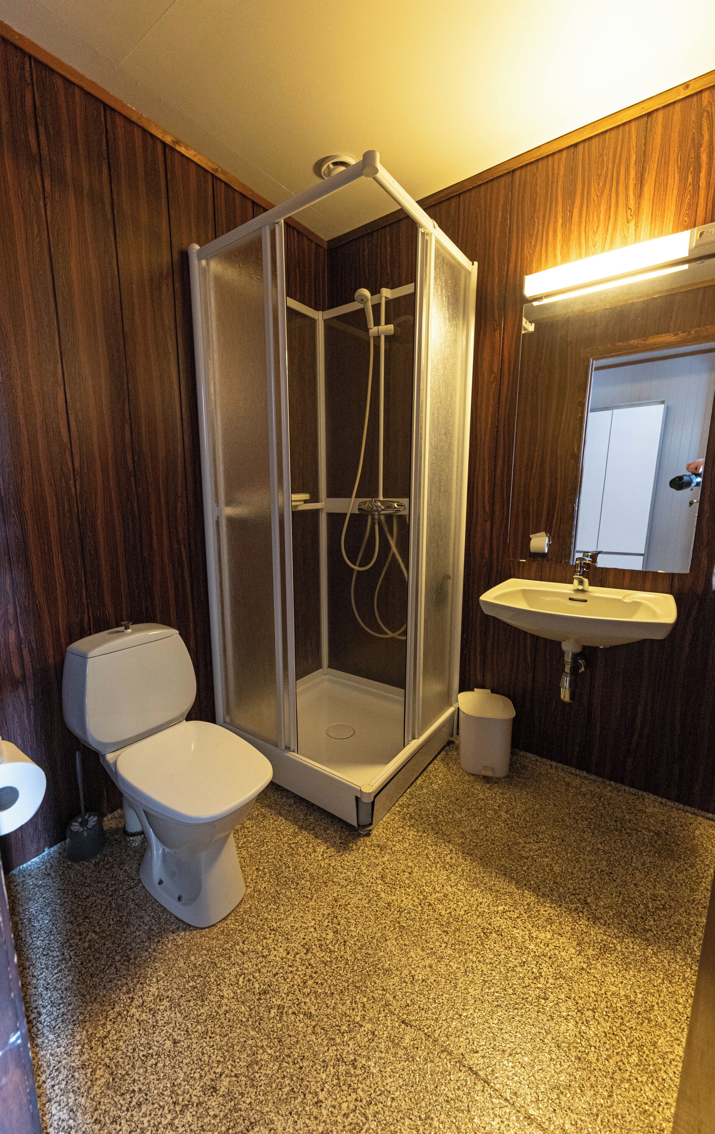 A bathroom with a shower enclosure, toilet, sink, and mirror.