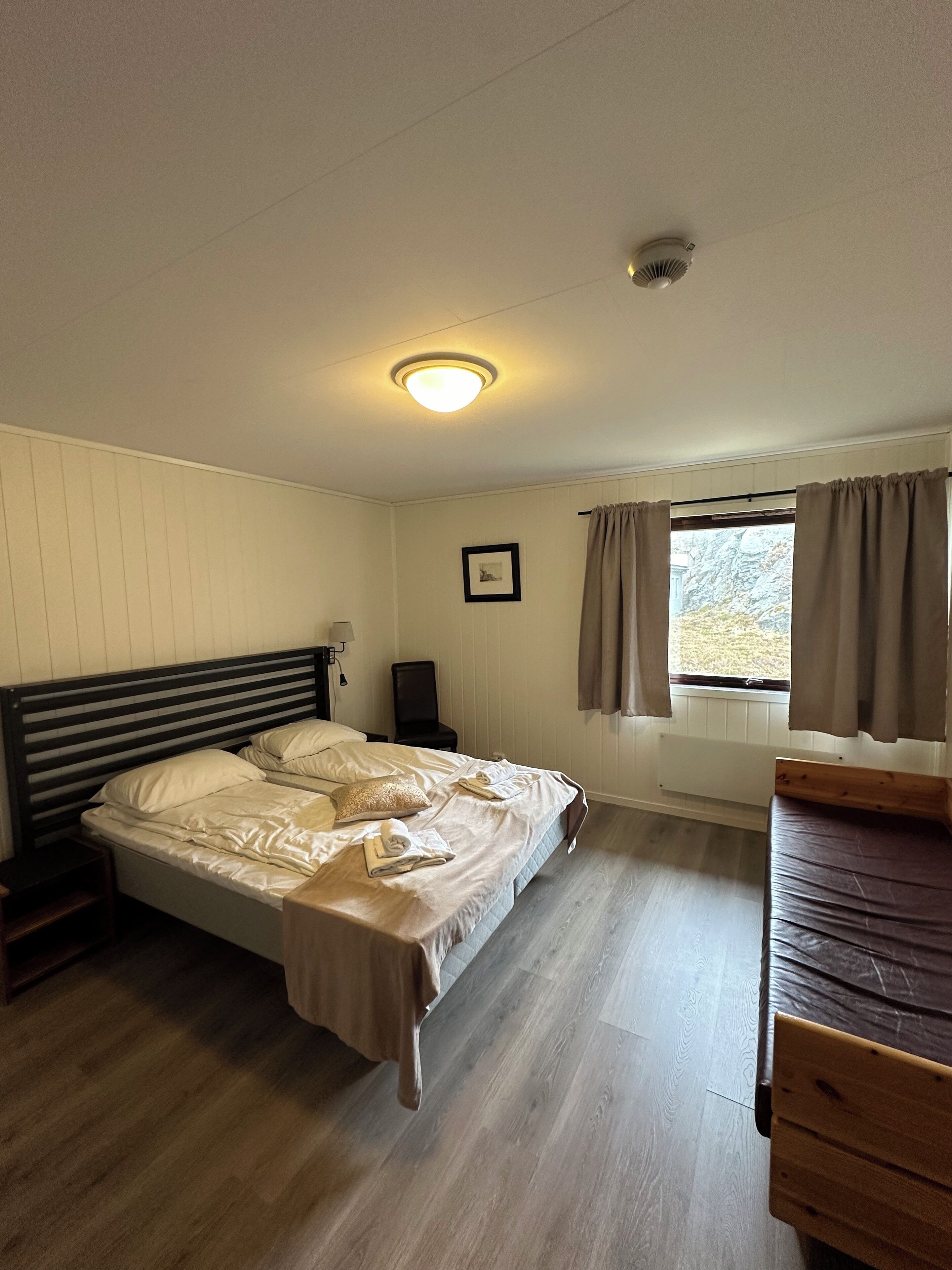 A bedroom with a bed, bedside tables, a window with curtains, and a radiator.