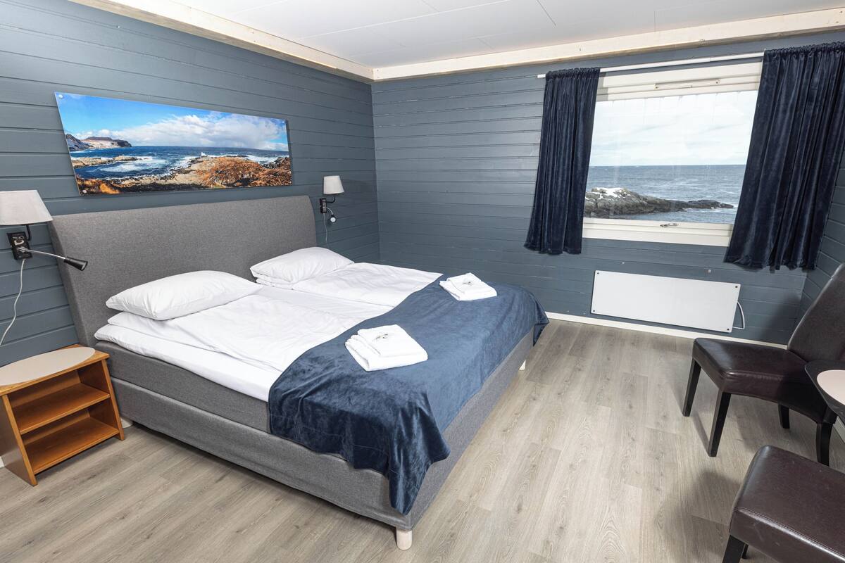 Quarto de hotel com cama, escrivaninha, cadeira, janela com cortinas e um quadro na parede.