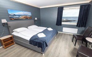 Habitación de hotel con cama, escritorio, silla, ventana con cortinas y un cuadro en la pared.