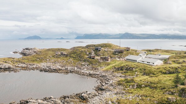 Una propiedad costera con varias construcciones, incluyendo una gran estructura blanca y varias casas más pequeñas, rodeada de terreno rocoso y una masa de agua.