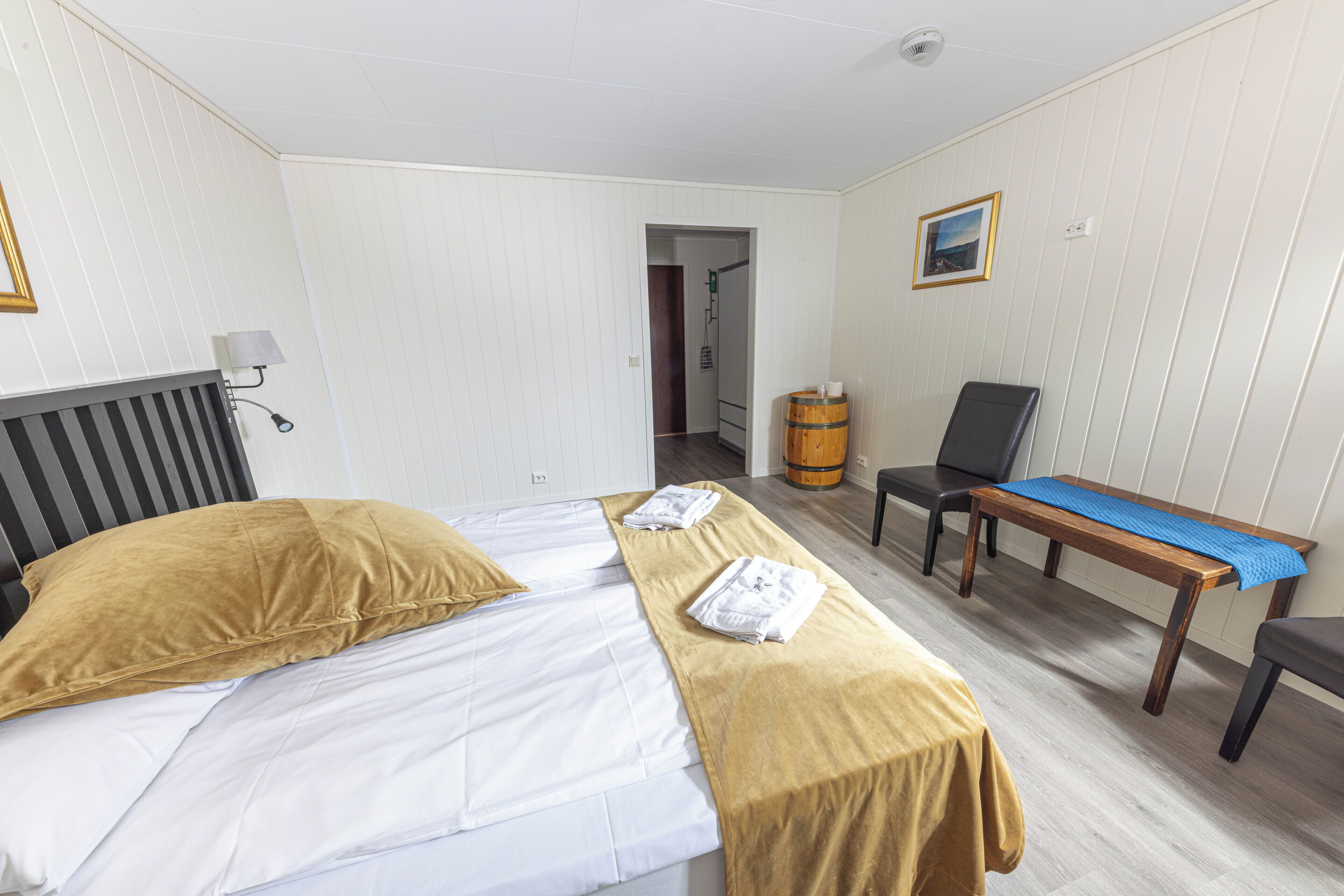 A hotel room with a bed, a chair, a table, and a picture on the wall.