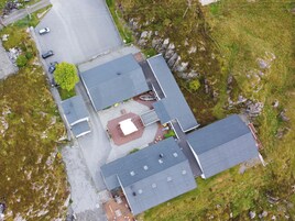 Vista aérea de un edificio con varios tejados, un camino pavimentado y un aparcamiento con coches.