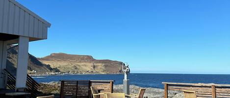 A wooden deck with wicker chairs and tables overlooking a coastal view.