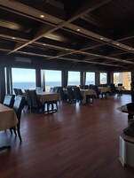 Un comedor amplio con mesas y sillas, ventanas grandes que ofrecen vistas al océano y un techo de madera.