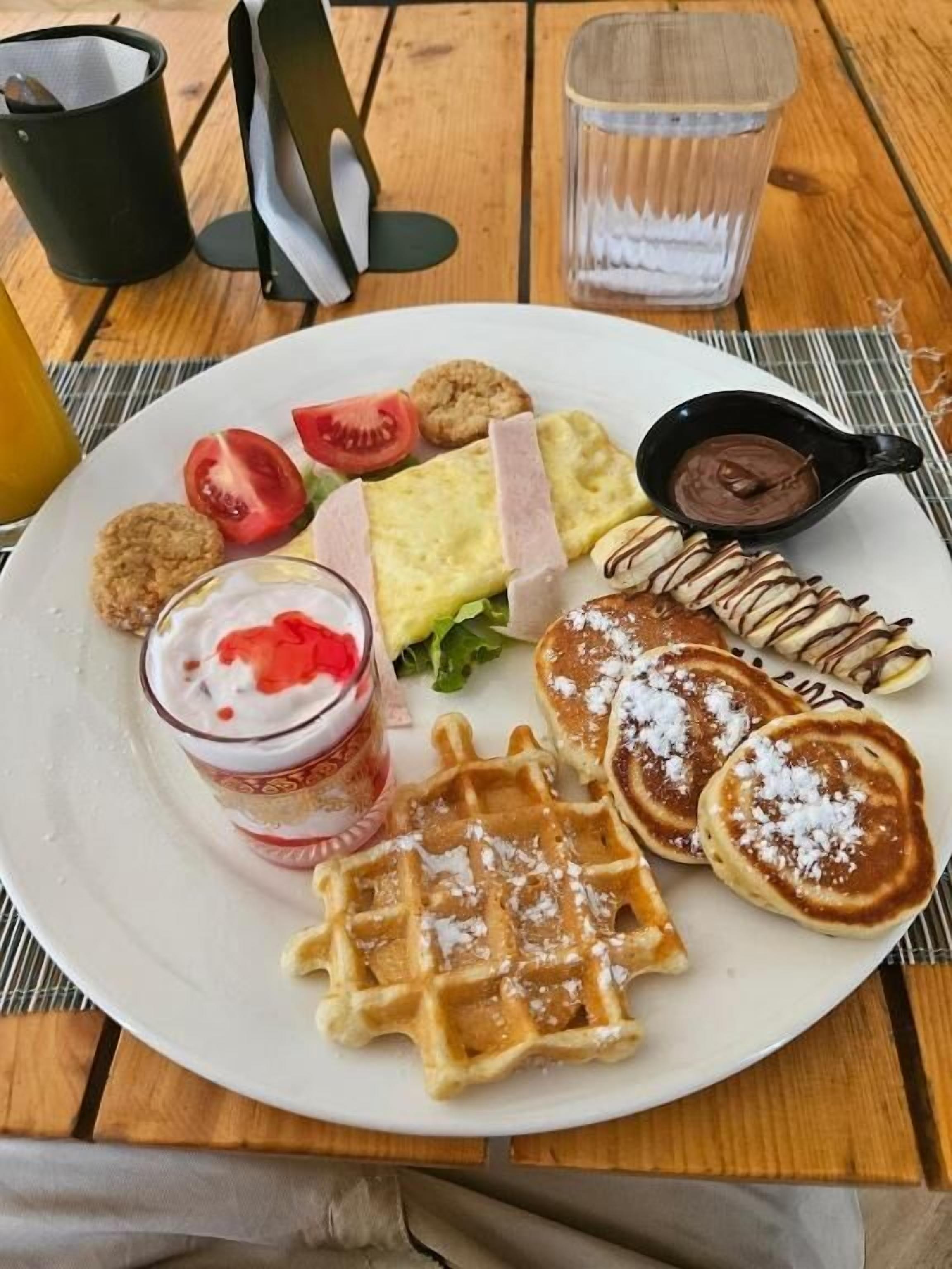 Um prato de comida com waffles, panquecas, um sanduíche e uma pequena tigela de molho de chocolate.