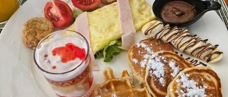 Um prato de comida com waffles, panquecas, um sanduíche e uma pequena tigela de molho de chocolate.