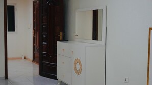 Un aparador blanco con espejo y un motivo circular decorativo, ubicado frente a una pared blanca en un pasillo con piso de baldosas.