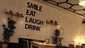 Un rincón comedor acogedor con mesas y sillas de madera, una pared con la inscripción "SMILE EAT LAUGH DRINK" y plantas en macetas.