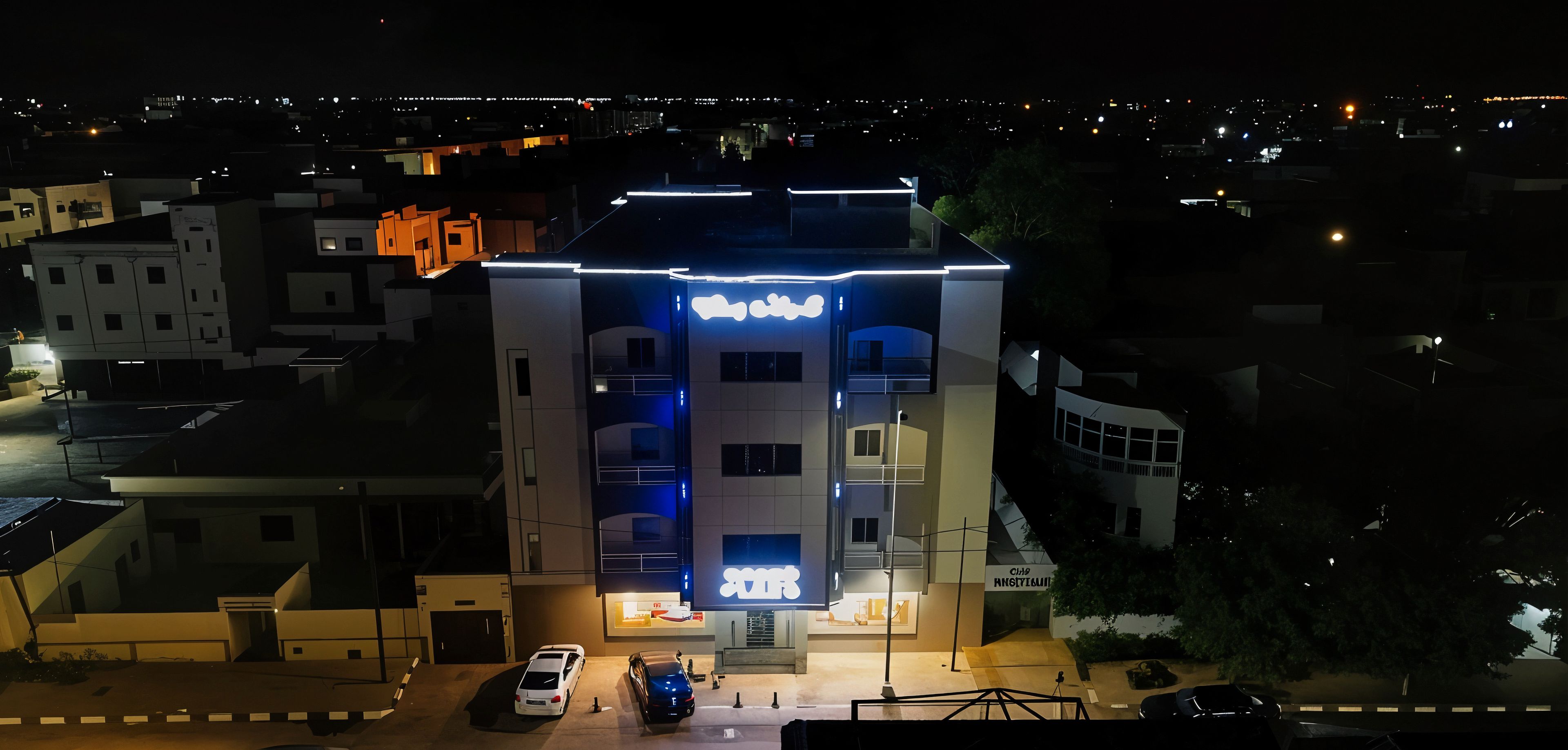 A multi-story hotel with illuminated signage, a parking area, and surrounding buildings.