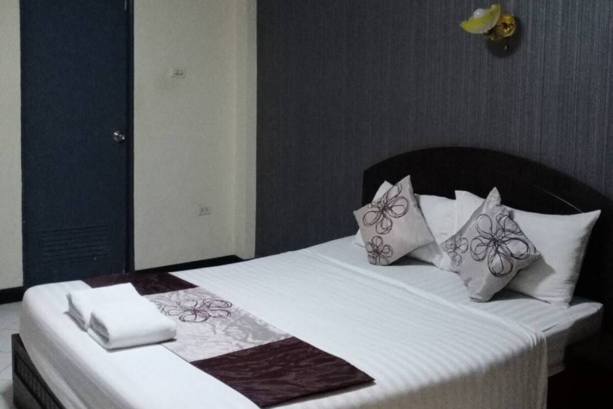 A neatly made bed with white linens and decorative pillows, a dark headboard, and a small wall-mounted light fixture.