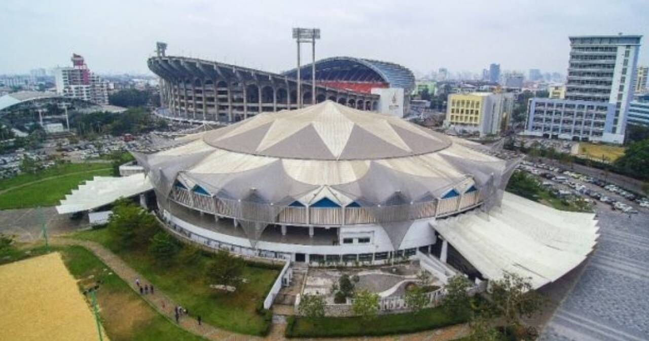 A stadium with a unique geodesic dome structure, surrounded by urban buildings and a parking area.