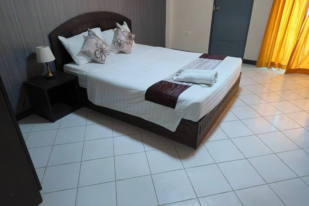 A neatly made bed with white linens and decorative pillows, a bedside lamp, and a wooden headboard.