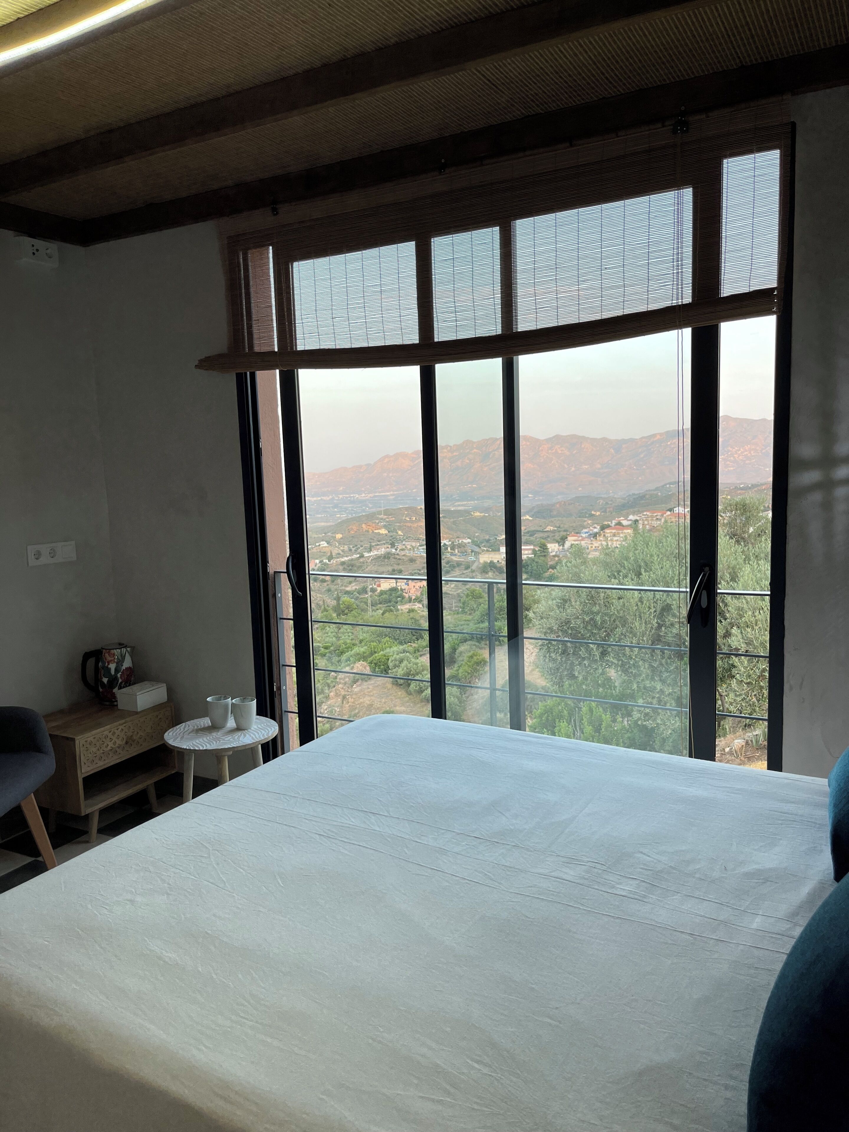 Une chambre avec une grande fenêtre, un lit, une petite table et une chaise.