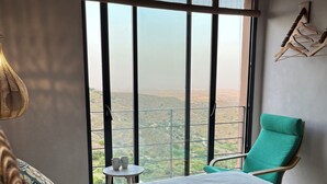 Une chambre à coucher avec un grand lit, un fauteuil vert et une vue sur un paysage, visible à travers une grande fenêtre.