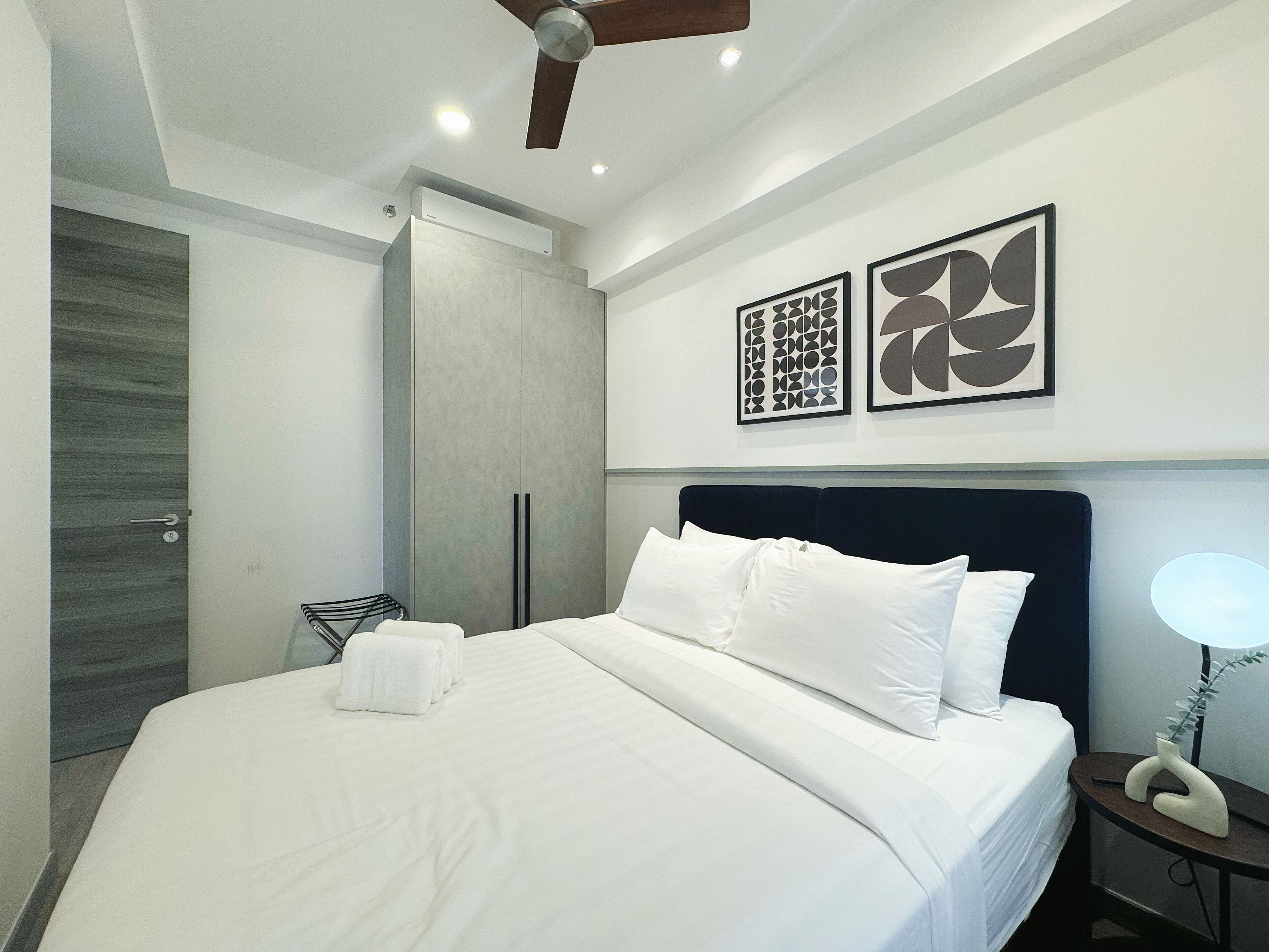 Une chambre d’hôtel moderne dotée d’un grand lit, d’un ventilateur de plafond et d’œuvres d’art abstraites sur les murs.