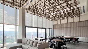 Een ruime zithoek met een royale hoekbank, meerdere tafels en stoelen, met een modern plafondontwerp en grote ramen met uitzicht op de stad.