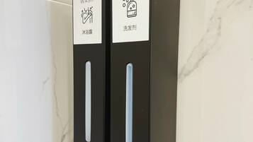 Two black dispensers with labels for body wash and shampoo, mounted on a white tiled wall.