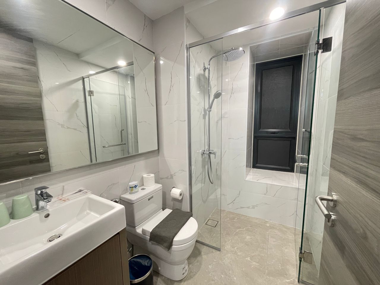 Un baño moderno con ducha de mampara de vidrio, un lavamanos blanco y un inodoro.