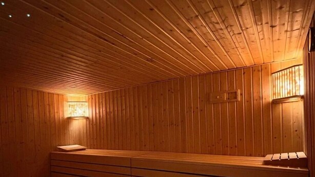 A sauna with wooden walls and benches, equipped with wall-mounted lamps. - Ferienhaus, 90m², 1-8 Pers (Rheine)