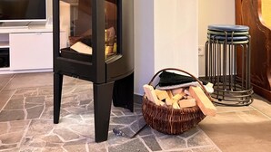 A modern living room with a black wood-burning stove, a stone-tiled floor, a television, and a wooden chair. - Ferienhaus, 90m², 1-8 Pers (Rheine)