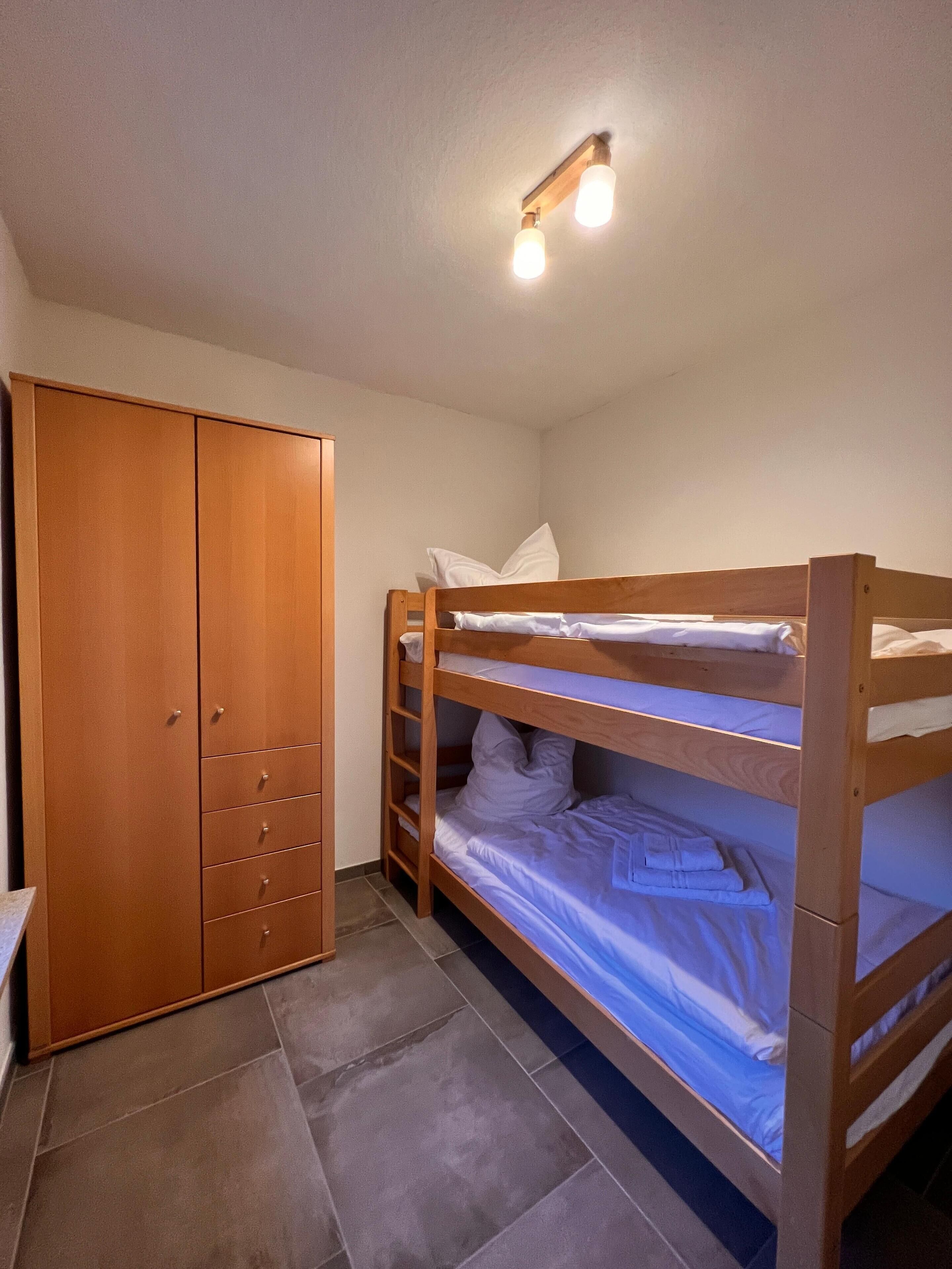 A bunk bed room with a wooden wardrobe and a ceiling light fixture.