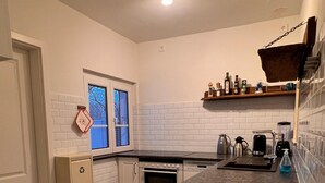 A compact kitchen with white cabinetry, a built-in oven, a coffee maker, and a window with a view of trees. - Ferienhaus, 90m², 1-8 Pers (Rheine)