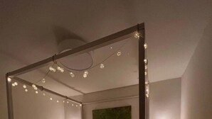 A four-poster bed with white linens, two bedside tables with lamps, and string lights. - Ferienhaus, 90m², 1-8 Pers (Rheine)